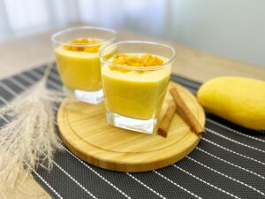Two glasses of creamy mango lassi garnished with diced mango and cinnamon sticks.