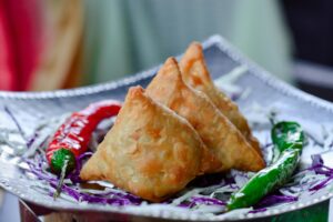 Crispy Indian samosas served with chili peppers and cabbage garnish.